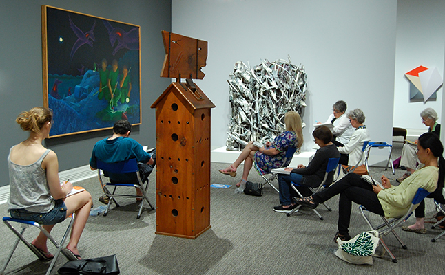 Adults sitting on stools and drawing in a gallery