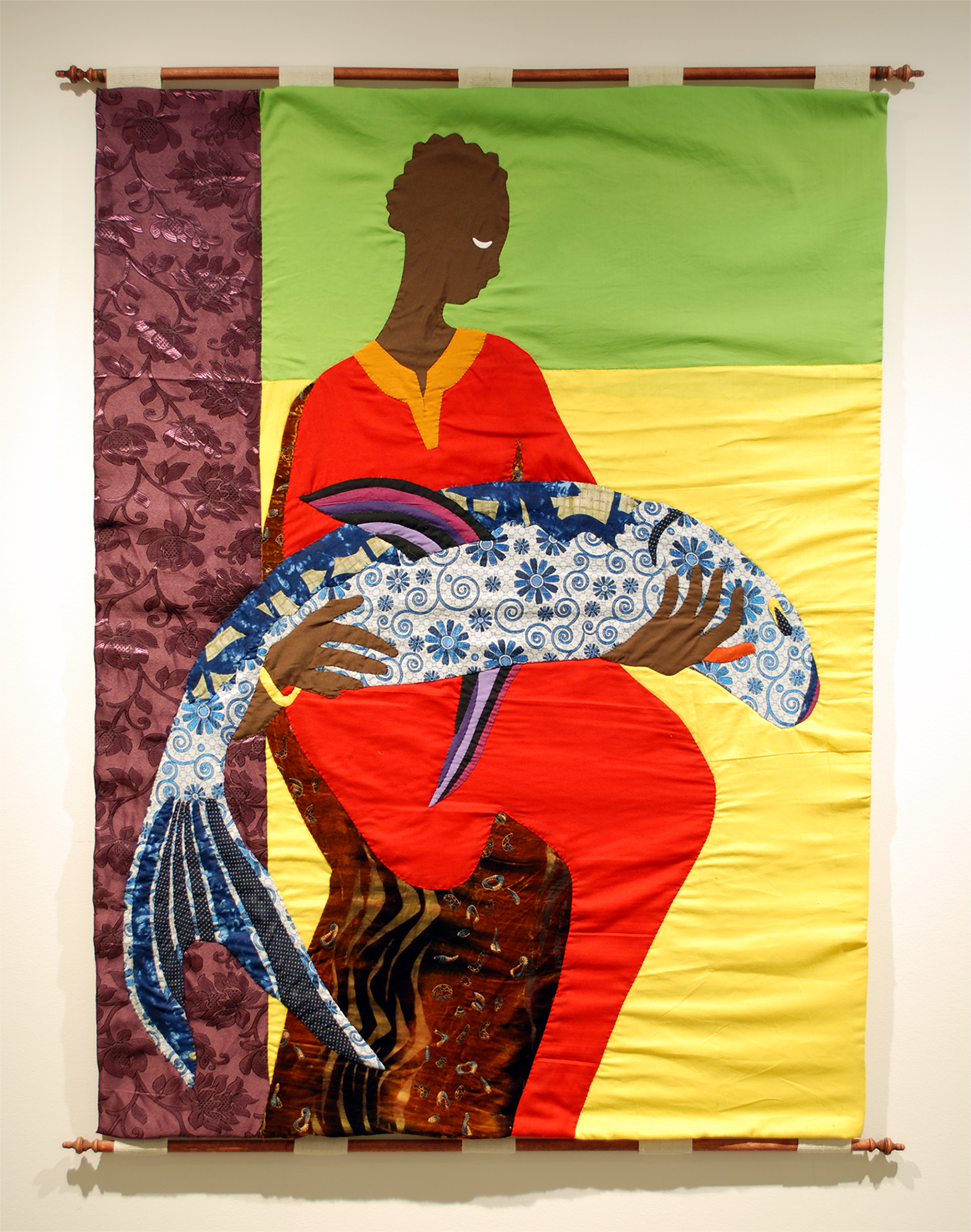 Image of tapestry work by Christopher Myers featured image of Black woman in a red dress holding a large blue and white fish. The background features a embroidered purple stripe on the left and a horizontal lime green stripe at top right with yellow rectangle filling the remainder of the background. The work is hung on wooden dowels.